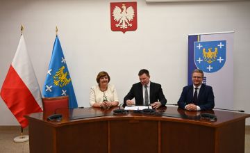 Trzy osoby siedzące za biurkiem podpisujące umowę